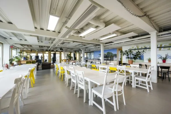 Moderne en ruime kantine met witte tafels en stoelen, gele accenten en veel planten aan de James Wattstraat.